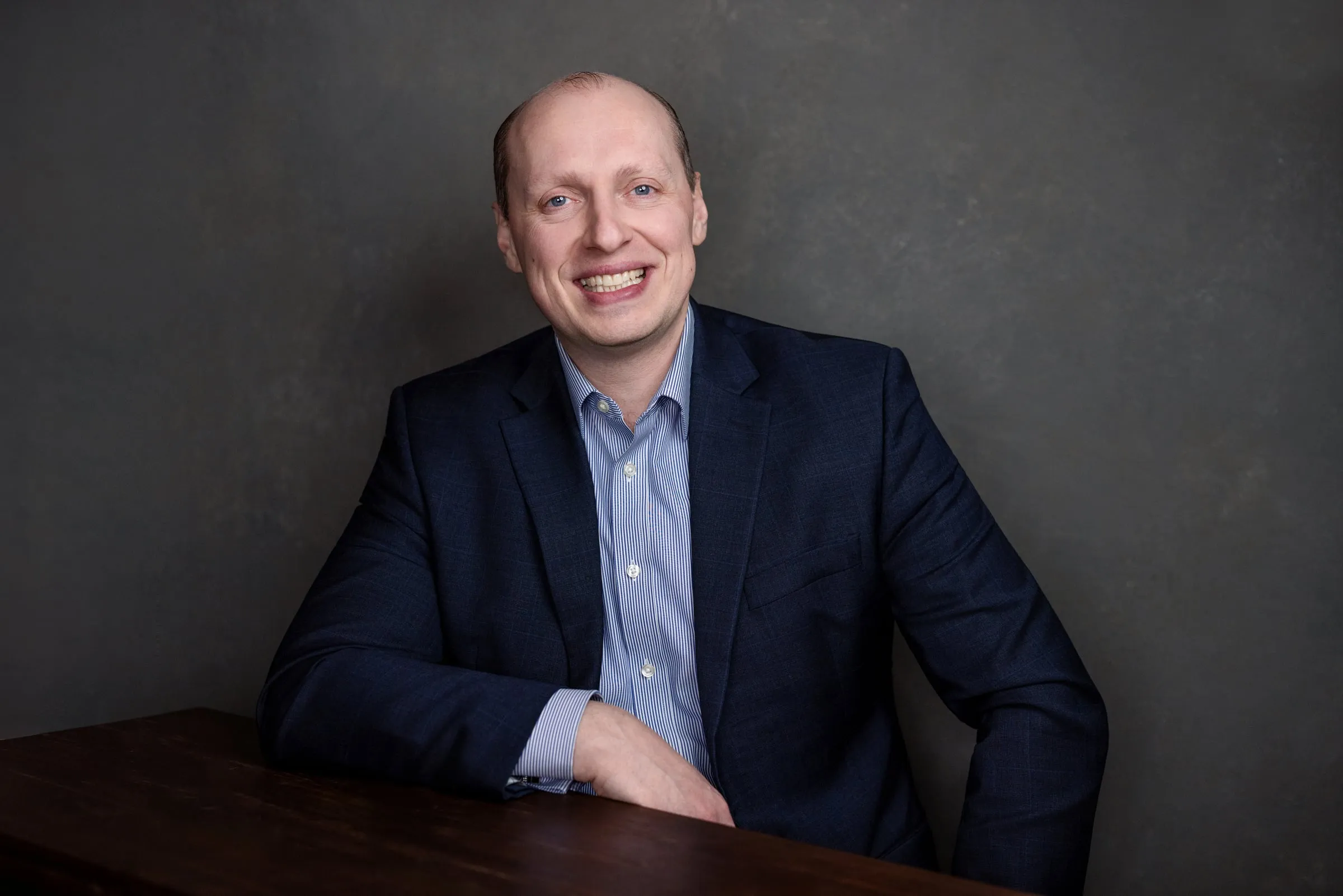 Yuriy Demidko leaning on a table, smiling, against a dark backdrop